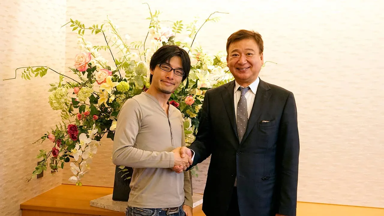 アレンジメントフラワーの前で株式会社Cerevo代表取締役社長と握手をして記念撮影