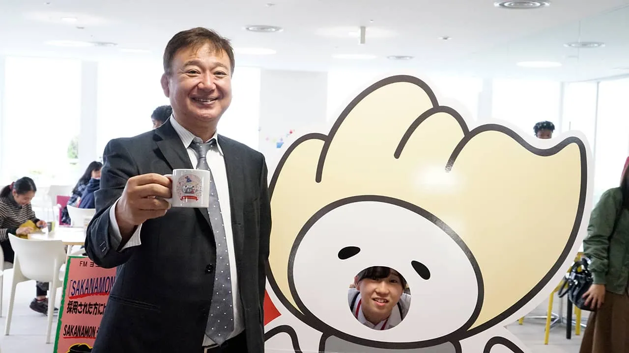 マグカップを手に、顔出しパネルから顔を出している学生スタッフと1枚