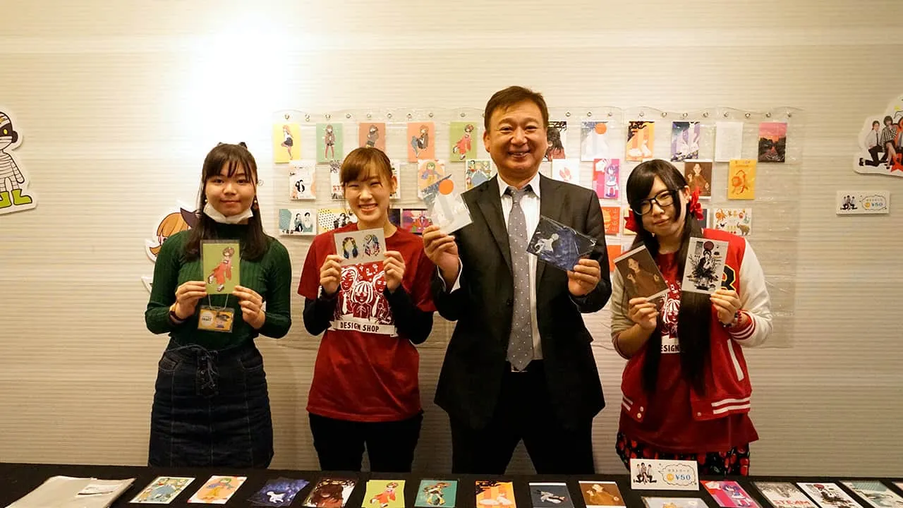 葉書サイズのデザインカードを持って担当の学生達と