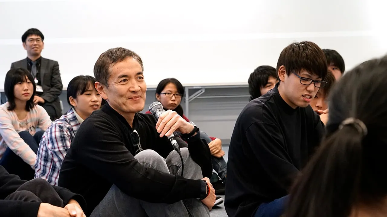 学生達の中に並んで座り、嬉しそうにマイクを持っている特別講師の様子