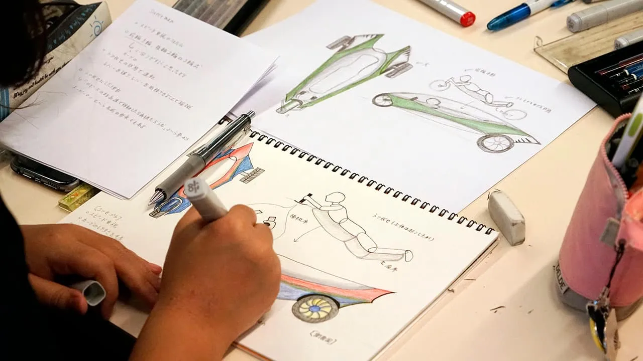 2枚の絵を並べ、メモを横に置いて線画に色を付けている手元