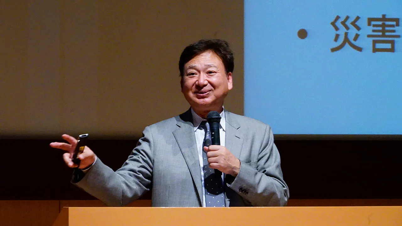 リモコンを持った出てジェスチャーをしながら講義を行う校長