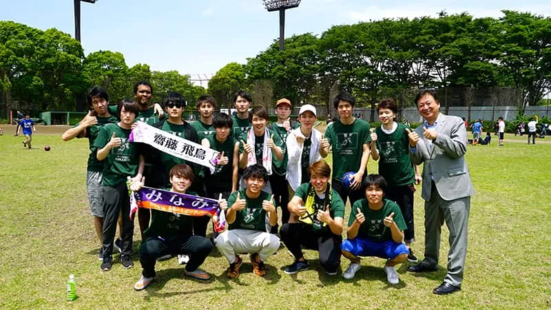 緑のお揃いTシャツを着たデザインカレッジ学生のみなさんと千葉理事長
