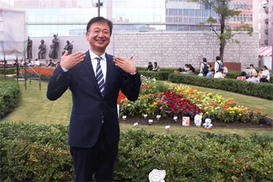 フラワーガーデンのきれいな花畑をバックに笑顔で写る千葉理事長