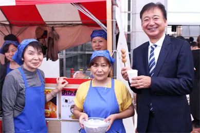 お団子を片手に蒲田西口町会のみなさんと笑顔で記念撮影する千葉理事長