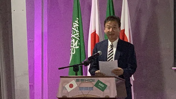 双方の国旗をバックに祝辞を述べる千葉理事長