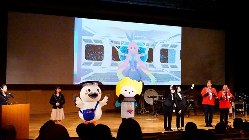 壇上で生徒2人が学園のゆるキャラたちと共に宣言する姿