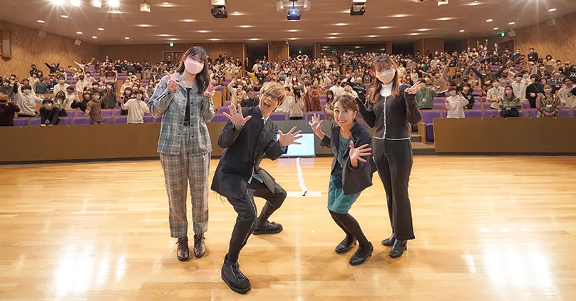 大勢の学生をバックに壇上から撮影した山寺さん、富永先生、学生2人