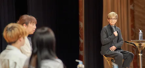 壇上でトークする山寺さんと富永先生を見つめる生徒2人