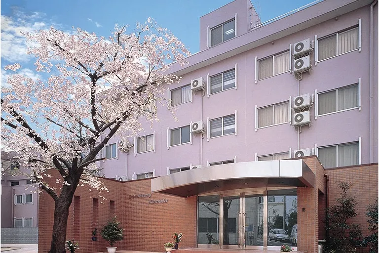 桜のシンボルツリーとレンガ調のエントランスを持つ桜色の外観