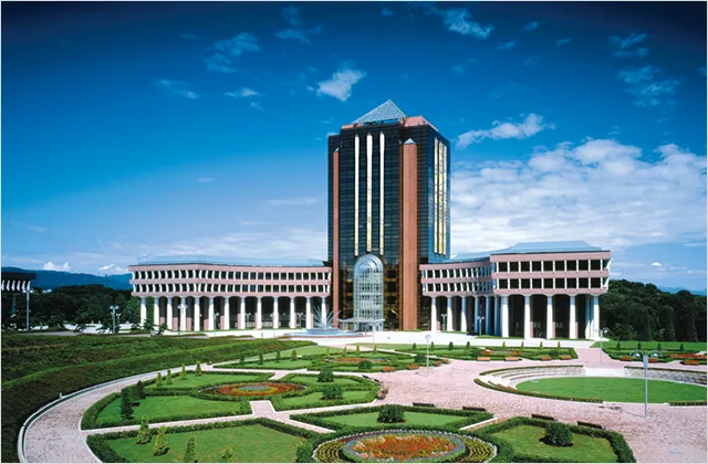 広大な庭園の奥にガラス張りのビルを中心にして、半円を描くようにギリシャ式の建物が広がる片柳研究所棟