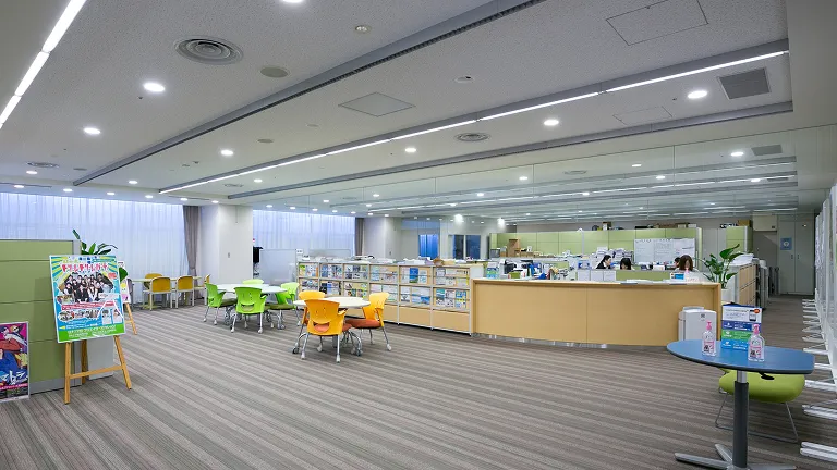 丸テーブルと緑やオレンジの椅子のセットが配置され、カウンターでオープン型のオフィスが仕切られたリラックスできる空間の画像