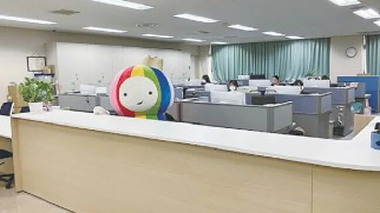 オープン型のオフィスの受付カウンターの奥に大きなマスコットキャラクターのぬいぐるみが見える風景