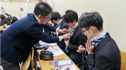 学生たちがスーツのネクタイを締めている様子