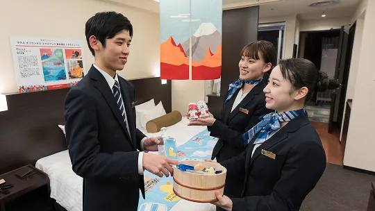 学生たちがホテル客室でアメニティ用品を手渡しながら打ち合わせをしている様子