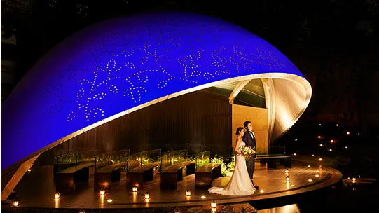 曲線的にデザインされた青い屋根の下でキャンドルライトに照らされたステージと新郎新婦