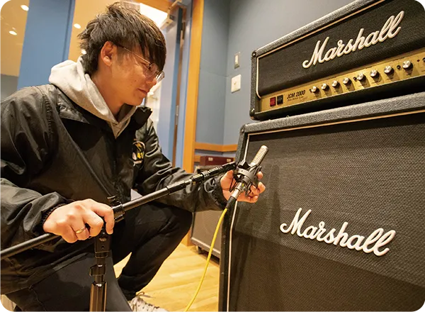 ギターアンプにマイクをセットする学生の様子