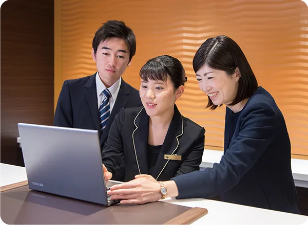 フロント研修でPC画面を見ながら説明を受ける学生たち