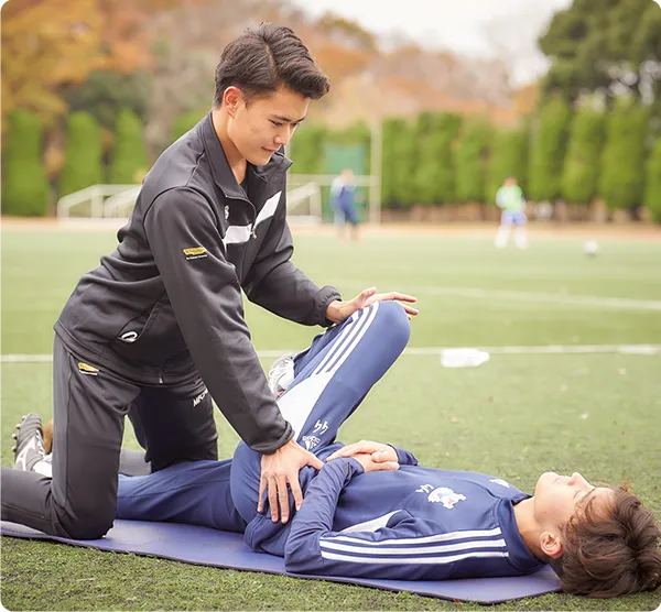 屋外で選手にストレッチを行う学生