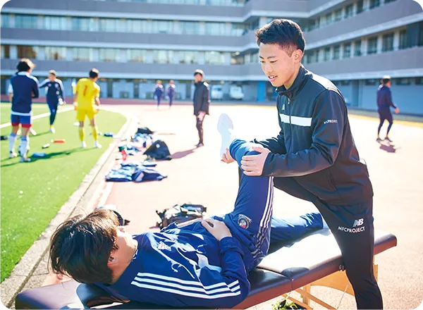グラウンドで選手のストレッチを行う学生