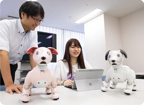 ２体の犬型のロボットを見つめる学生と講師の様子