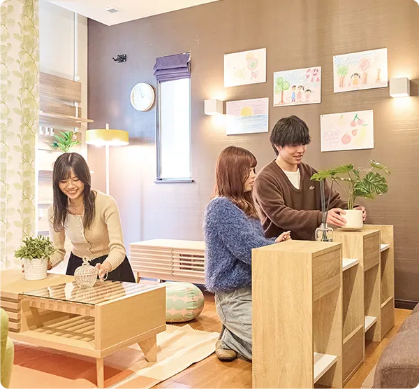 ３名の学生が屋内で観葉植物や小物を配置している様子