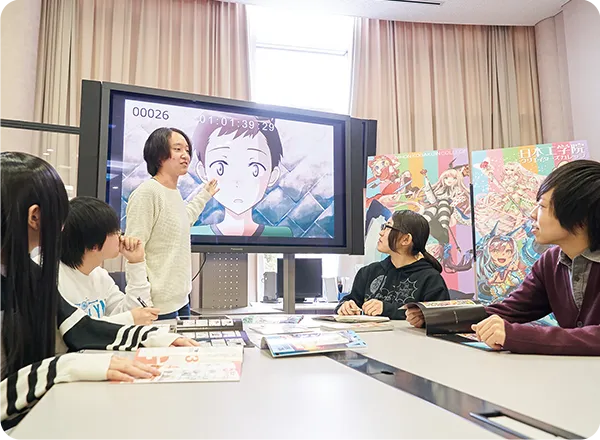 複数の学生がモニターのアニメーションを見て議論する様子