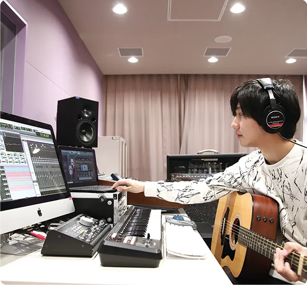 学生がスタジオでギターを抱えて機材を操作している様子