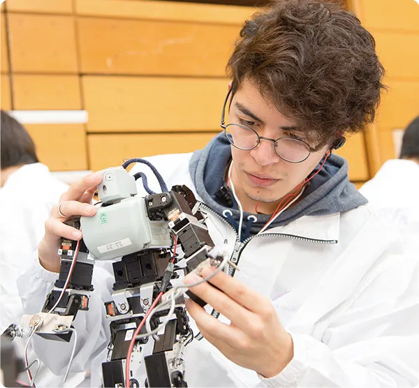 人型ロボットとイヤホンを接続し、それを耳にしながらロボットを触る学生