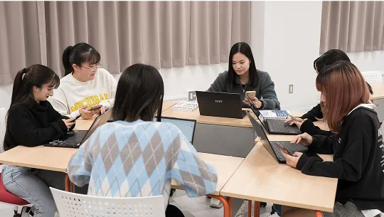学生グループがスマートフォンやパソコンを使用する様子