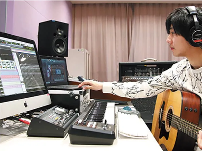 ギターを抱えたままパソコン操作をしている学生