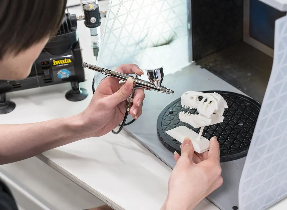 恐竜の化石の模型にエアーブラシを吹きかける学生