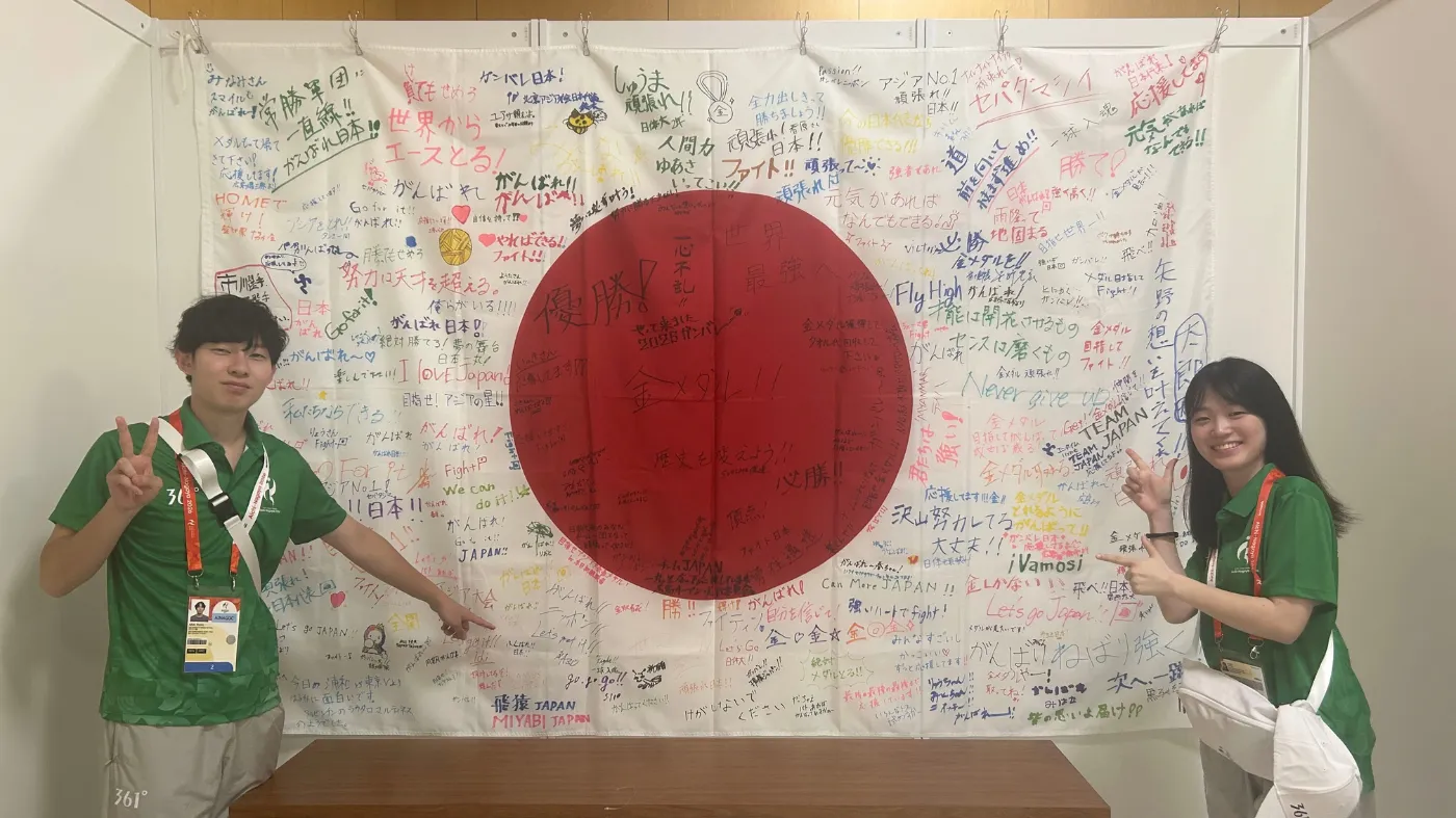 応援メッセージで埋め尽くされた日の丸の寄せ書きパネルの前で記念撮影する2人。