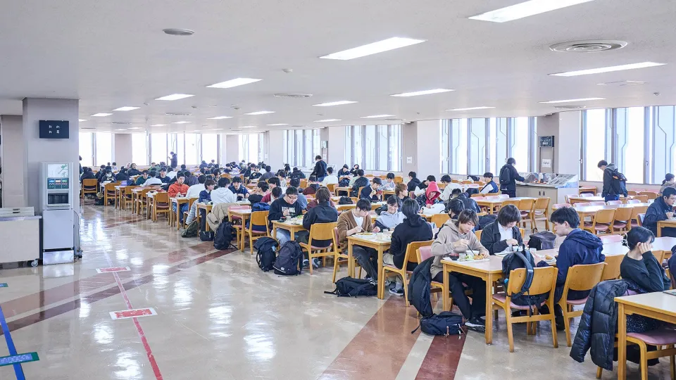木製のテーブルと椅子が並んだ食堂で生徒達が食事をしている画像