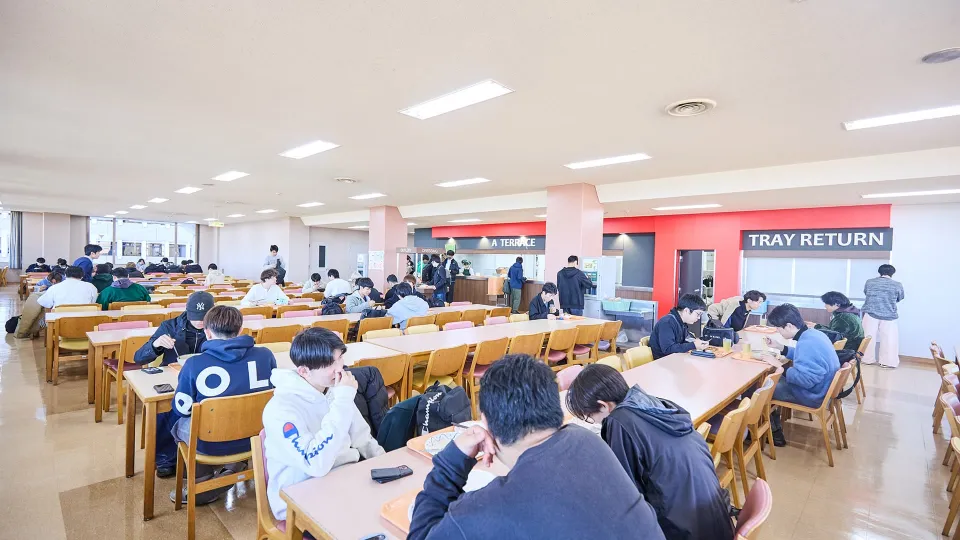 窓に囲まれ明るい光が差し込むとても広い食堂の画像