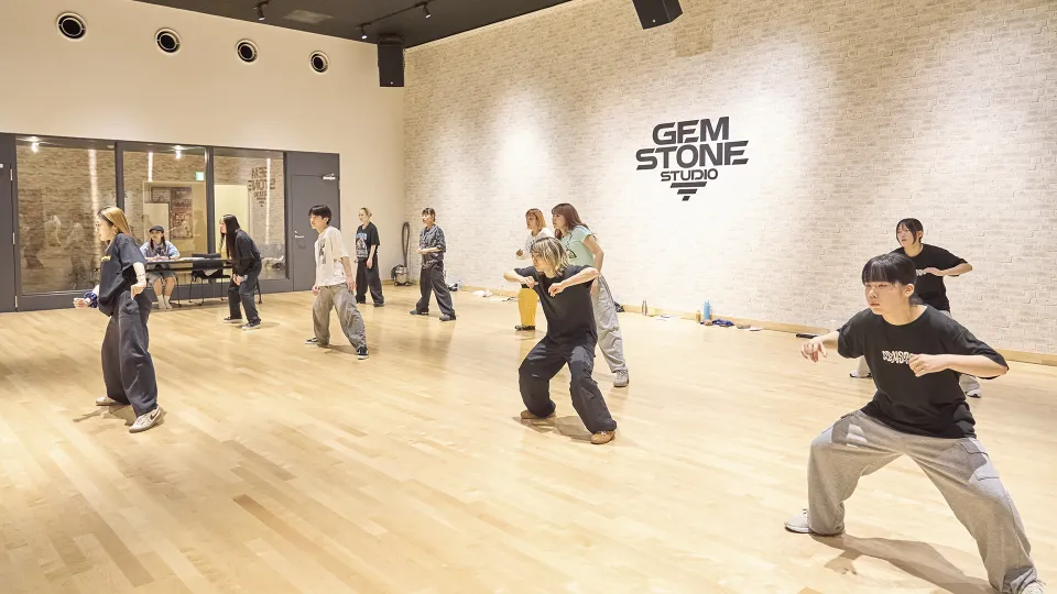 明るいスタジオ内で真剣にダンスのレッスンをする学生たち