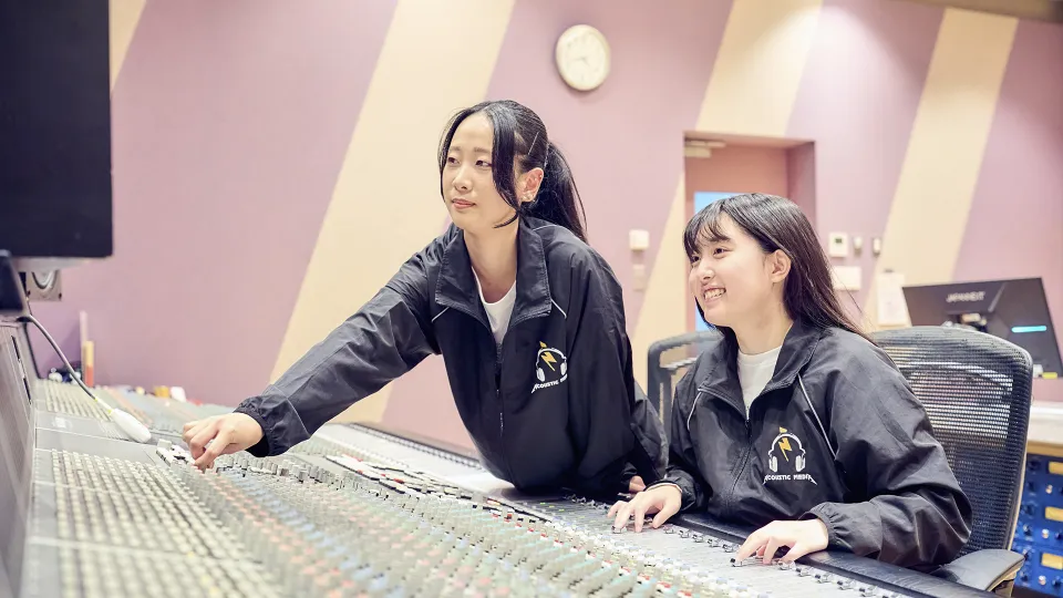 コントロールルームでミキサーを楽しそうに操作する2人の学生