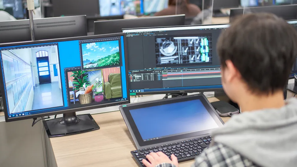 パソコンとタブレットを使い、アニメの背景画を制作する学生